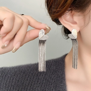 Close-up of elegant long silver tassel earrings with a sparkling heart-shaped stud on model