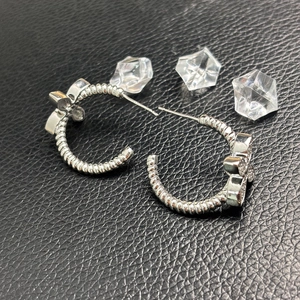 Sparkling butterfly C-shaped silver earrings with twisted rope texture on black leather
