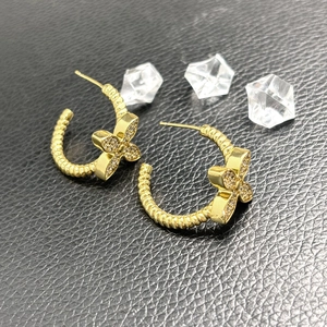 Macro shot of gold C-shaped twisted hoop earrings with a sparkling floral crystal stud