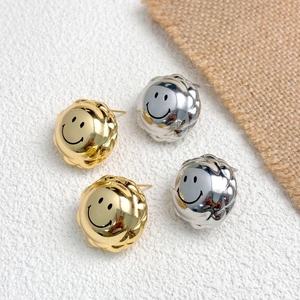 Detail of gold and silver smiley face stud earrings with quilted texture on white sand