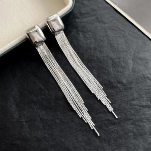 Detailed view of silver chain tassel earrings with rectangular studs on a dark texture