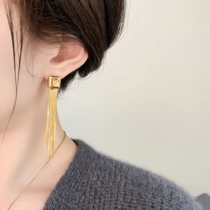 Close-up of golden tassel earrings with square studs worn by a model in a minimalist setting
