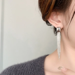 Close-up of elegant silver long chain tassel earrings worn on a model with knitwear