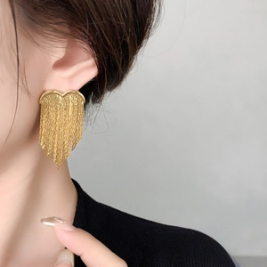 Detailed close-up of golden heart tassel earrings with dangling metallic fringe on a model