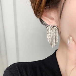 Close-up of silver heart-shaped tassel earrings worn by a model in a minimalist setting