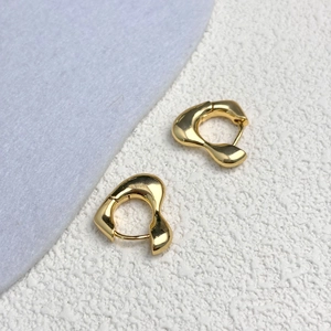 Détail macro de boucles d'oreilles cœur dorées polies avec texture de lave fluide