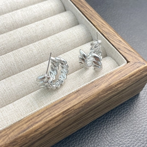 Elegant silver C-shaped oval hoop earrings with woven texture on wooden jewelry tray