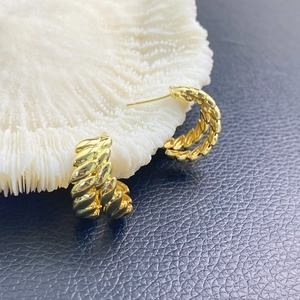 Golden chunky oval hoop earrings with twisted woven texture on white coral stone background