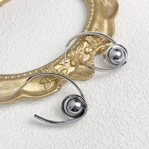 Detailaufnahme silberner Spiral-Ohrringe auf weißem Stein mit antikem goldenem Rahmen