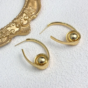 Minimalistische Spiral-Creolen mit Goldperle auf texturiertem weißem Hintergrund