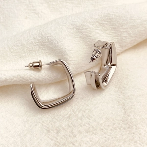 Minimalist square geometric earrings in polished silver finish on textured fabric