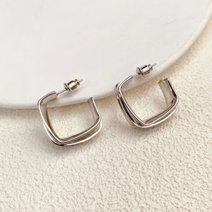 Macro shot of silver geometric square earrings with a polished finish on white ceramic