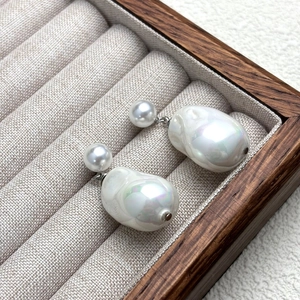 Baroque pearl earrings featuring small round pearls and large iridescent drop pearls on wood