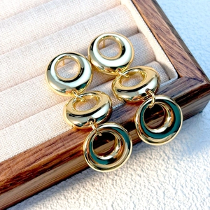 Close-up of three-tier gold circular drop earrings in a textured wooden jewelry box