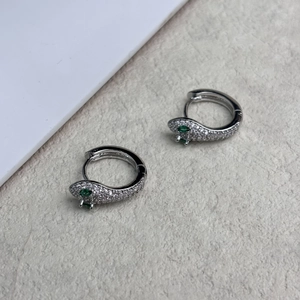 Détail macro de boucles d'oreilles serpent argentées avec cristaux et yeux vert émeraude
