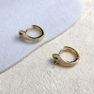 Détail de boucles d'oreilles serpent en or avec zircons sertis et yeux en pierres vertes