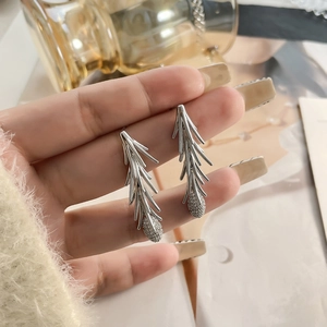 Elegant silver pine branch tassel earrings with white zircon accents held by hand