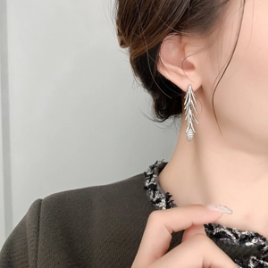 Close-up of silver floral tassel earrings with pine branch design on model wear