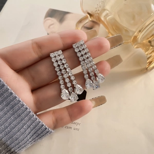 Long silver tassel earrings with white zircons and pear-shaped drops held by a hand