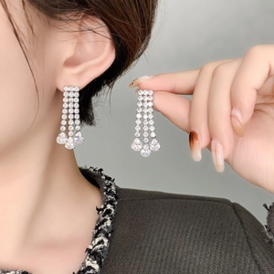 Close-up of sparkling silver tassel earrings with round and teardrop zircons on model