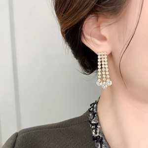 Close-up of dangling gold-plated earrings with three-row tassels and pear-shaped rhinestones