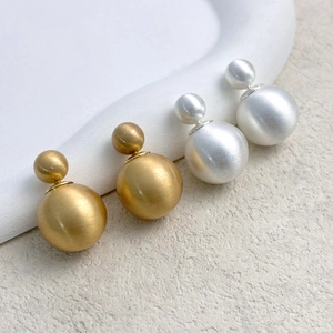 Detail of brushed metal double ball earrings in gold and silver finish with matte texture