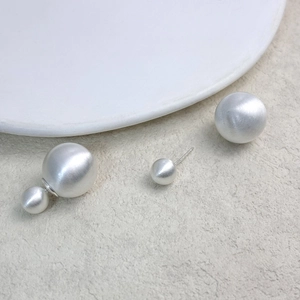 Detail of matte silver brushed metal double-sided sphere stud earrings on a textured surface