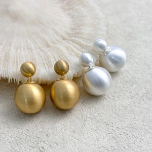 Detail of gold and silver brushed metal double ball earrings with matte texture finish