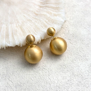 Minimalist matte gold double ball stud earrings shown on white coral display stand