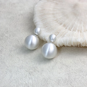 Macro shot of matte white double-bead earrings on textured coral and stone background