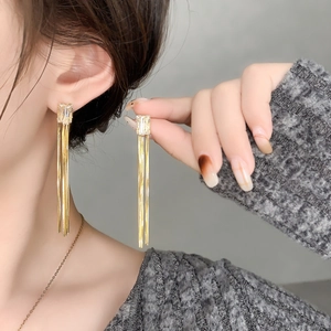 Détail de boucles d'oreilles longues dorées à glands avec zircon rectangulaire