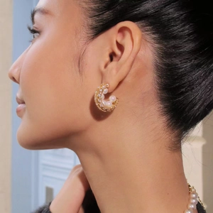 Detail of C-shaped 18K gold earrings featuring pavé set pearls and cubic zirconia on model