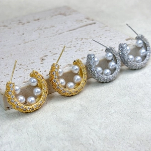 Detailed macro view of 18K gold and silver C-shaped earrings with pearls and micro zircons