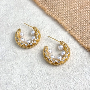 Detail of C-shaped gold-plated earrings with white pearls and sparkling zircons