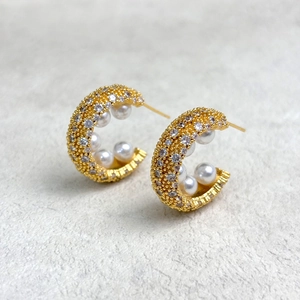 Detailed macro view of 18K gold C-shaped hoop earrings with pearls and pavé cubic zirconia