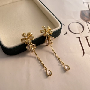 Detail of long gold-plated bow tassel earrings with micro-set zircons and pear crystals