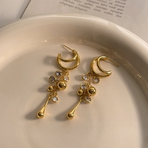 Close-up of 18K gold plated C-link tassel earrings with cubic zirconia on ceramic plate