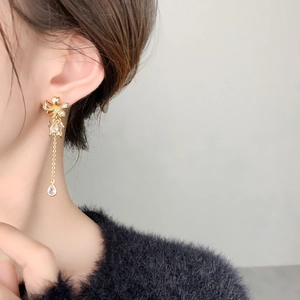 Detail of gold bow earrings with long tassel chain and teardrop zircon drop on model