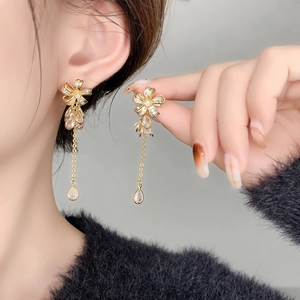 Detailed view of long gold-plated floral earrings with crystal tassels on a model