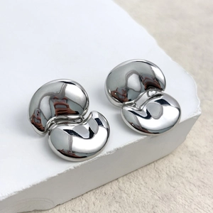 Macro detail of minimalist polished silver bean earrings on white stone texture