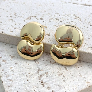 Macro detail of gold geometric bean earrings on travertine stone showing polished finish