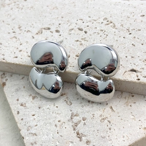 Modern polished silver bean shaped earrings displayed on a minimalist travertine stone