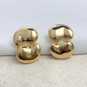 Detailed close-up of polished gold bean-shaped drop earrings on white textured surface