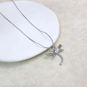 Close-up of a silver dragonfly pendant with sparkling zircons on a white ceramic plate
