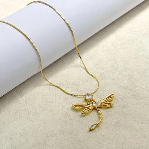 Elegant gold dragonfly necklace with sparkling crystal wings on a minimalist white stand