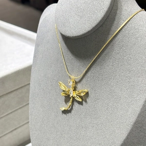 Elegant gold dragonfly necklace with hollow wings and inlaid gems on a gray display stand