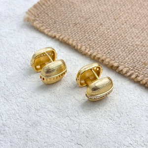 Detail of gold huggie earrings with brushed metal texture and zircon micro-inlay