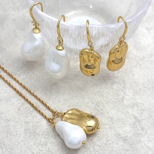 Détail d'un ensemble collier et boucles d'oreilles en perles baroques sur fond gris texturé