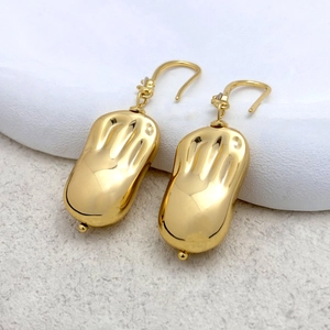 Détail de boucles d'oreilles dorées en forme de cacahuète avec texture ondulée sur pierre
