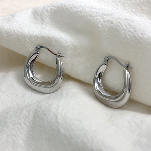 Minimalist U-shaped earrings in polished silver finish on white textured fabric background